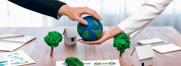 Business people holding paper earth together over office table. Green corporate company implementing eco-friendly policy to reduce CO2 emission and conserve green environment concept. Trailblazing