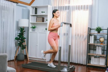Enerjik ve güçlü atletik Asyalı kadın evde koşu makinası çalıştırıyor. Formda fiziğin takibi ve ev çalışması ve eğitimle sağlıklı yaşam tarzına bağlılık. Kuvvetli