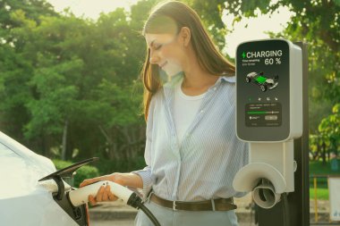 Yolculuk sırasında doğal ormanlarda ya da güneş ışığı alan ulusal parklarda elektrikli araba için şarj olan genç bir kadın. Tatil ve tatil boyunca çevre dostu seyahat. Yükselt