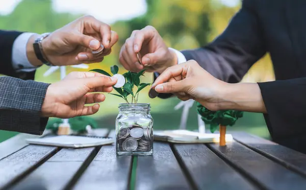 Business people put coin to money saving glass jar on outdoor table as sustainable money growth investment or eco-subsidize. Green corporate promot and invest in environmental awareness. Gyre
