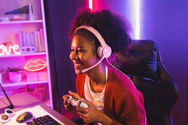 Oyun flamasının sunucu kanalı, Esport yetenekli takım oyuncusuyla yarışan Afrikalı kız ve neon renkli aydınlatma odasında online oyun izleyicileri. Siber spor ev içi aktiviteleri kavramı. Tatlandırıcı.
