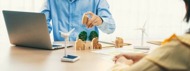 İki iş adamı yeşil iş toplantısında yenilenebilir enerji, ahşap ev bloğu ve ağaç modeli temsil edilen yel değirmeni ile toplantı masasında Eko şehrinden bahsediyorlar. Tanımlama.