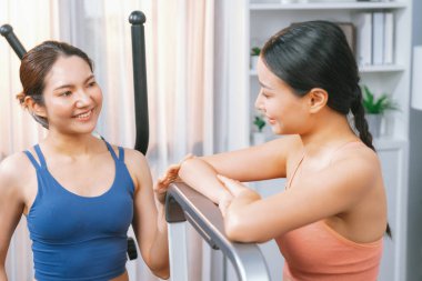 Enerjik ve güçlü atletik Asyalı kadın evde spor arkadaşı ya da antrenörü ile birlikte eliptik koşu makinesiyle koşuyor. Formda fiziğin takibi ve sağlıklı yaşam tarzına bağlılık. Kuvvetli