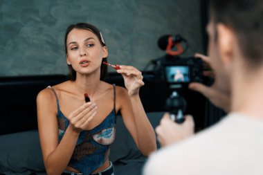 Genç bir kadının sosyal medya için güzellik ve kozmetik dersi videosu çekmesini videoya çeken bir adam. Güzellik blogcusu kameraya gülümserken seyircilere ve takipçilere güzellik bakımını gösteriyor. Açılıyor