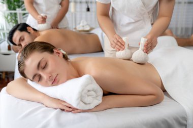 Sıcak bitkisel top spa masaj vücut tedavisi, masör nazikçe bitki torbasını çift müşteri vücuduna bastırıyor. Aromaterapi dinlenme sükuneti ve sükuneti kaplıca salonundaki atmosferi aydınlatıyor. Sessiz.