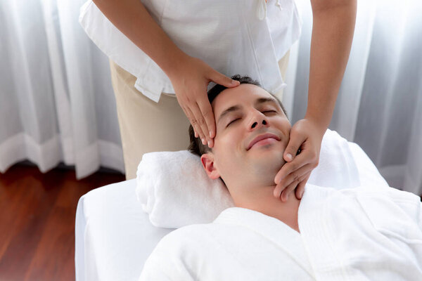 Кавказский мужчина наслаждается расслабляющим анти-стрессовым массажем головы и расслабляющим отдыхом кожи лица в дневном спа современном светлом окружении на роскошном курорте или в спа-салоне отеля. Quiescent