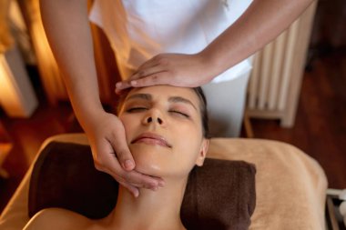 Beyaz kadın stres önleyici kafa masajı yapmaktan ve lüks otel veya otelde sıcak mum ışığında yüz güzelliği eğlencesi yapmaktan zevk alıyor. Sessiz.