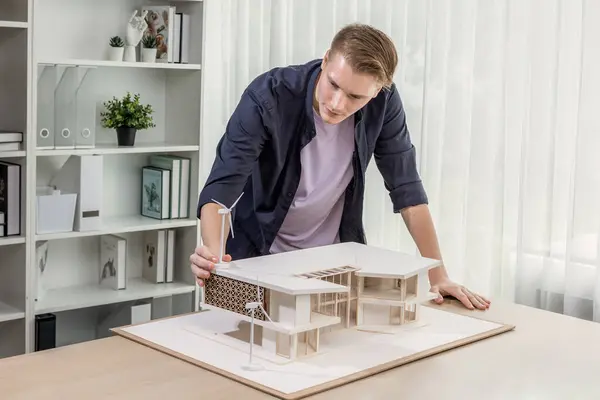 Architect designer studies elegant house model, reviewing structure design for improvement with construction plan on table. Creativity and innovation in architectural design. Iteration