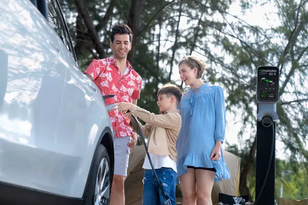 stock image Outdoor adventure and family vacation camping in nature travel by eco friendly car for sustainable future. Lovely family recharge EV car with EV charging station in campsite. Perpetual