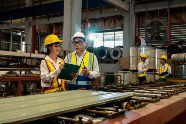 Fabrika mühendisi, metal levha ürünü üzerinde kalite kontrolü yapmak ve ağır endüstriyel çelik damgalama veya oluşturma makinesini denetlemek için iş arkadaşıyla işbirliği yapar. Örnek gösteriliyor