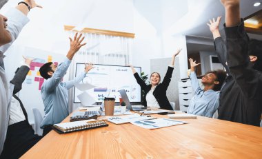 Bir grup ofis çalışanı toplantı odasında kutlama yapıyor, evrak işlerini havaya atıyorlar. İş adamlarından gelen heyecan ve özgürlük ifadesi, finansal analiz kağıtlarını kutlama jesti olarak fırlatıyor. Uyum