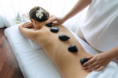 Lüks tatil köyündeki kaplıcalarda sıcak taş masajı. Gün ışığı sükunet ortamında, mutlu kadın müşteri bazalt taş masajından zevk alıyor. Rahatlatıcı bir sıcaklıkla vücudun üzerinde süzülüyor. Sessiz.