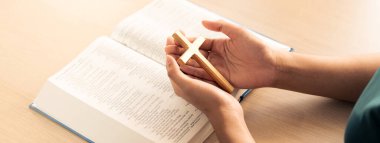 Dişi Tanrı inananı, açık ahşap kilise masasında kutsal kitap üzerinde ahşap haç tutuyor. Üst Manzara. Umut, din, inanç, Hıristiyanlık ve Tanrı 'nın kutsaması kavramı. Sıcak bir arka plan. Filizlenen.