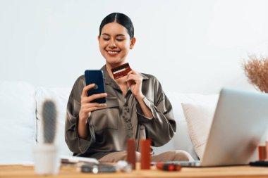 Genç mutlu Asyalı kadın internetten alışveriş yaparak ürün satın alırken aynı zamanda internetten kredi kartıyla online ödemeler sipariş ederek çevrimiçi mağaza platformundan en yüksek sanal güvenlik tarafından korunuyor.