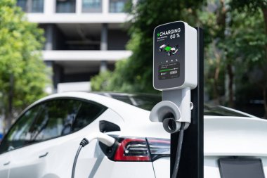 Yazın yeşil sürdürülebilir şehir bahçesinde elektrikli araba şarj oluyor. Kentsel sürdürülebilirlik yaşam tarzı yeşil temiz yeniden şarj edilebilir enerji elektrikli BEV araç iç organları