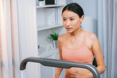 Enerjik ve güçlü atletik Asyalı kadın evde koşu makinası çalıştırıyor. Formda fiziğin takibi ve ev çalışması ve eğitimle sağlıklı yaşam tarzına bağlılık. Kuvvetli