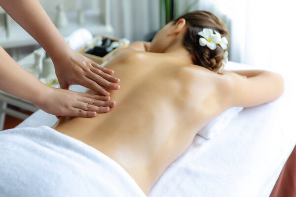 Caucasian woman customer enjoying relaxing anti-stress spa massage and pampering with beauty skin recreation leisure in day light ambient salon spa at luxury resort or hotel. Quiescent