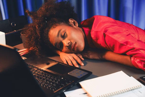 African woman freelancer feeling tried and take a nap on desk around by laptop and stationary, waiting for proceed project job until sleeping on desk. Concept of work life at home place. Tastemaker.