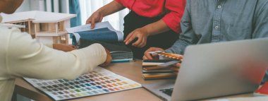 Yetenekli iç dizayn ekibi perde malzemelerini dikkatle seçerken iş arkadaşı da toplantı masasının üzerinde ev modeliyle perdenin rengini seçiyor. Yaratıcı tasarım konsepti. Değiştirilmiş.