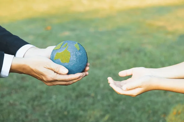 Businessman hand giving Earth globe to little boy as Earth day concept as corporate social responsible to contribute greener environmental protection for sustainable future generation. Gyre