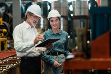 Metal imalatında makine mühendisliği denetleyicisi olarak liderlik örneğini sunan çelik endüstriyel makineyi incelemek için dizüstü bilgisayar kullanan fabrika mühendisi ve asistan..