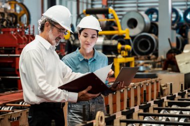 Metal imalatında makine mühendisliği denetleyicisi olarak liderlik örneğini sunan çelik endüstriyel makineyi incelemek için dizüstü bilgisayar kullanan fabrika mühendisi ve asistan..