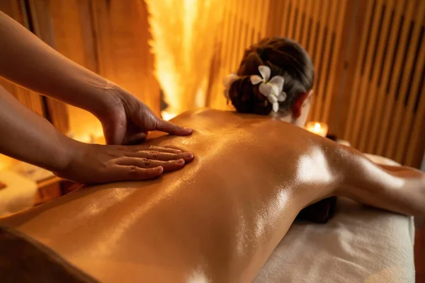 Closeup woman customer enjoying relaxing anti-stress spa massage and pampering with beauty skin recreation leisure in warm candle lighting ambient salon spa at luxury resort or hotel. Quiescent