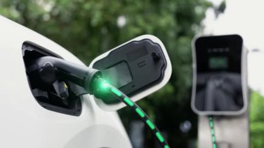 Elektrikli araba, doğal parktaki temiz enerji şarj istasyonundan gelen fütürist akıllı EV şarj cihazının dijital batarya durumu hologramıyla şarj oluyor. Gelecekçi çevre dostu EV araba. İnceleyin