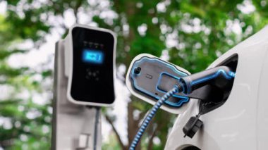 Doğal yeşil araba parkındaki ekolojik temiz enerji şarj istasyonundan gelen fütürist akıllı EV şarj aletinin şarj ettiği elektrikli araba. Alternatif enerji kullanan gelecekçi çevre dostu elektrikli araba. İnceleyin
