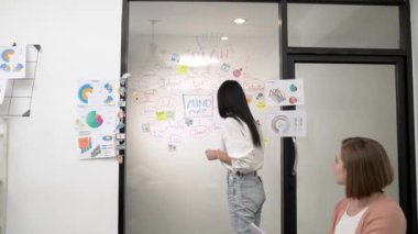 İş toplantısında zihin haritası, istatistiksel grafik ve renkli yapışkan notlar kullanarak cam tahtada yazarken yaratıcı pazarlama projesini sunan güzel beyaz iş kadını. Tertemiz..