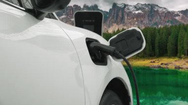 Temiz çevre için temiz enerjinin yol açtığı ilerici elektrikli araba kavramının arka planı olarak dağın tepesinde bulutun zaman kavramının yer aldığı doğal manzara. EV araba şarj istasyonunda şarj oluyor..