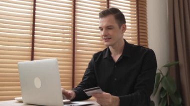 Genç adam internet bankacılığı için kredi kartlı dizüstü bilgisayar kullanıyor. İnternet üzerinden alışveriş yapıyor. Banka kartıyla modern ve kullanışlı online satın alma. Düzenle