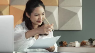 Güzel genç mimar mühendisinin portresi ev modelini ölçerken aynı zamanda dizüstü bilgisayar, proje planı ve masanın üzerine yerleştirilmiş taslağı da alıyor. İş tasarımı konsepti. Yönlendirici.