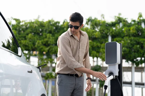 年轻人从室外绿城公园的充电站给电动汽车充电 可再生能源电动汽车促进可持续的环境友好型城市旅游生活方式 — 图库照片