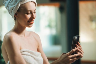 Beyaz havlu giymiş güzel tenli beyaz bir kadının portresi. Geleneksel spa salonunda gülümseyen yüzüyle fotoğraf çekiyor. Kaplıca kızı cep telefonuyla oynuyor. Huzur.