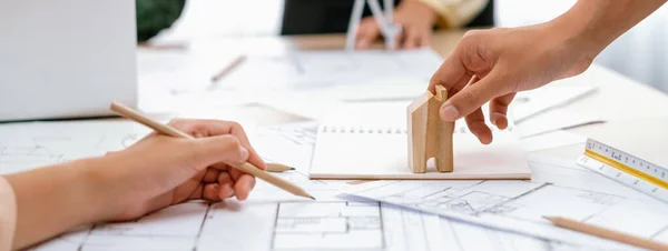 Professional architect team discussion about architectural project on meeting table with blueprint and wooden block scatter around at modern office. Closeup. Focus on hand. Delineation.