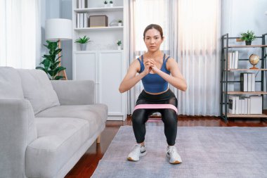 Güçlü enerjik kadın bacak kası kazanmak için direnç bandıyla evde egzersiz yapıyor. Genç atletik Asyalı kadın dayanıklılığı ve dayanıklılık antrenmanı..