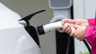 Modern çevre dostu kadın EV şarj istasyonundan elektrikli aracı şarj ediyor. EV araba teknolojisi ev sakinleri için gelecekte çevresel sürdürülebilirlik için kullanılıyor. Panorama Eşzamanlaması