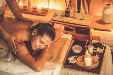 Caucasian woman customer enjoying relaxing anti-stress spa massage and pampering with beauty skin recreation leisure in warm candle lighting ambient salon spa at luxury resort or hotel. Quiescent clipart