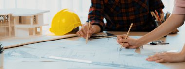 Kooperatif mimar ekibinin kesilmiş görüntüsü ev modeli, güvenlik miğferi ve mimari planlarla toplantı masasında birlikte çalışmaya karar verir ve birlikte çalışırlar. - Yakın çekim. Eline odaklan. Filizlenen.