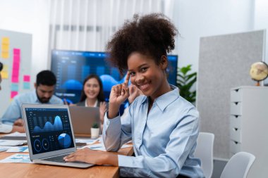 Bir grup ofis çalışanı ile birlikte arka planda ekranda gösterim paneliyle buluşan mutlu Afrikalı genç bir iş kadını portresi. Takım toplantısında kendine güveni tam bir ofis hanımı. Uyum