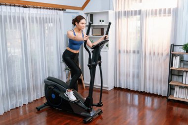 Enerjik ve güçlü atletik Asyalı kadın evde eliptik koşu makinesiyle koşuyor. Formda fiziğin takibi ve ev çalışması ve eğitimle sağlıklı yaşam tarzına bağlılık. Kuvvetli