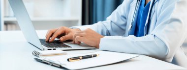 Hastanedeki doktor masasında oturup dizüstü bilgisayar üzerinde çalışıyor. Hasta test sonuçlarını teşhis ediyor, hastalıklar ve hastalıklar için tedavi planı geliştiriyor. Sağlık personeli ve sağlık hizmetleri. Panorama Katı