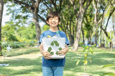 Neşeli Asyalı çocuk, elinde gündüz vakti elinde geri dönüşüm sembolü olan yeşil parkı tutarak atık geri dönüşümünü teşvik ediyor, azaltıyor ve gelecek nesiller için sürdürülebilir çevre farkındalığı için teşvikleri yeniden kullanıyor. Döngü