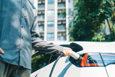 Genç adam yazın yeşil sürdürülebilir şehir bahçesinde EV elektrikli araba ile seyahat ederek yeşil, temiz, yeniden şarj edilebilir elektrikli araç iç organları ile kentsel sürdürülebilirlik yaşam tarzını gösteriyor