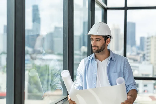 Professional architect engineer or male worker in casual outfit looking at skyscraper and city view while holding project plan. Creative design, civil engineering, building construction. Tracery.