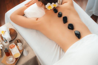 Lüks tatil köyündeki kaplıcalarda sıcak taş masajı. Gün ışığı sükunet ortamında, mutlu kadın müşteri bazalt taş masajından zevk alıyor. Rahatlatıcı bir sıcaklıkla vücudun üzerinde süzülüyor. Sessiz.