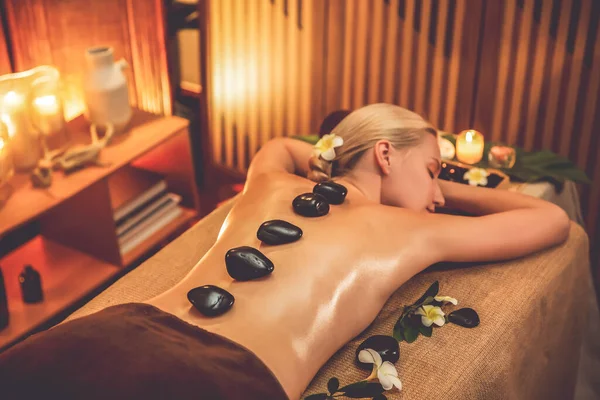 Lüks tatil köyündeki kaplıcalarda sıcak taş masajı, sıcak mum ışığı, spa bazalt taşı masajının keyfini çıkaran mutlu kadın müşteriler, rahatlatıcı bir sıcaklıkla vücudun üzerinde süzülüyorlar. Sessiz.
