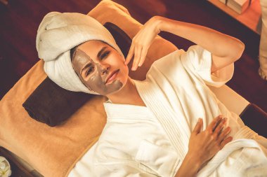 Kaplıca salonunun sakin atmosferi, üst düzey kadın müşteri sıcak mum ışığında kömür kömürü yüz kremi masajıyla kendini yenilemeye çalışıyor. Yüz bakımı ve güzellik konsepti. Sessiz.