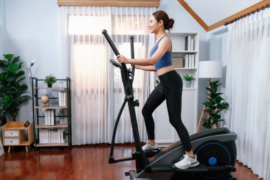 Enerjik ve güçlü atletik Asyalı kadın evde eliptik koşu makinesiyle koşuyor. Formda fiziğin takibi ve ev çalışması ve eğitimle sağlıklı yaşam tarzına bağlılık. Kuvvetli